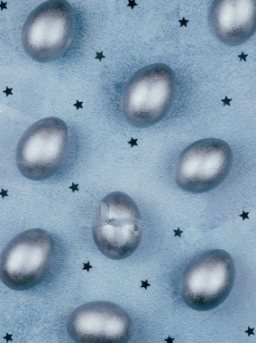 Gümüş renkli Paskalya yumurtaları mavi desenli arka planda yay ve yıldızlarla süslenmiş..