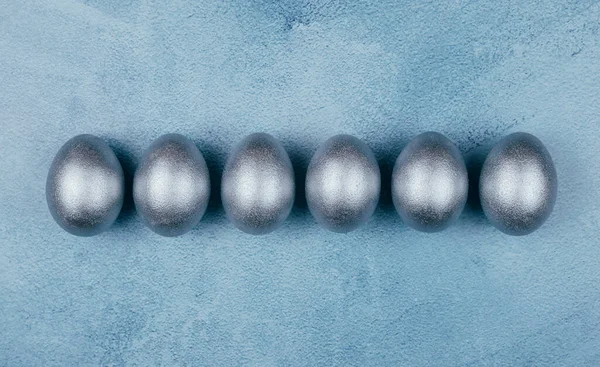 Ovos de Páscoa de cor cinza prata em uma fileira no fundo azul texturizado. Espaço de cópia . — Fotografia de Stock