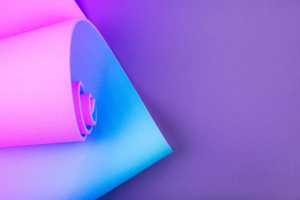 Mor arkaplanda neon renkli pembe yoga minderinin üst görüntüsü. Metin için boşluk.