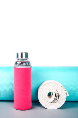 Bükülmüş mavi yoga minderi, kemer ve beyaz arka planda yeniden kullanılabilir cam su şişesi. Yoga pilates ya da fitness pratiği. Kilo vermek ve spor yapmak. Düz Yat. Boşluğu kopyala.