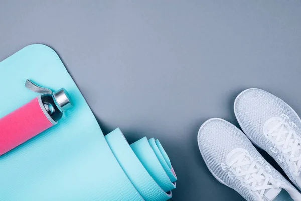 Beyaz spor ayakkabıları, mavi yoga minderi ve pastel gri arka planda yeniden kullanılabilir cam su şişesi. Yoga pilates ya da fitness pratiği. Kilo vermek ve spor yapmak. Düz Yat.