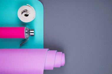Mavi yoga minderinin üst görüntüsü, cam su şişesi ve gri arka planda bükülmüş beyaz kemer. Yoga pilates pratiği, rahatlama ve meditasyon aksesuarları. Kilo vermek ve spor yapmak. Düz Yat.