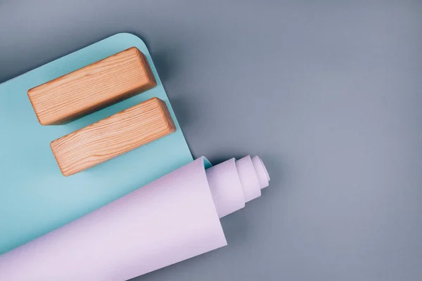 Mavi pembe yoga minderinin üst görüntüsü ve pastel gri arka planda iki tahta blok. Yoga pilates sporu konsepti. Düz Yat. Boşluğu kopyala.