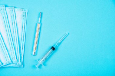 Mavi arka planda tek kullanımlık tıbbi koruyucu yüz maskesi, şırınga ve cıva termometresi. Virüs ve grip kavramı veya Coronavirus Covid-19, 2019-nCoV tedavisi. Boşluğu kopyala.