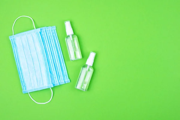 Yeşil arka planda tek kullanımlık iki tıbbi koruyucu yüz maskesi ve yeşil arka planda el dezenfektanı için antibakteriyel antiseptik sprey. Virüse karşı koruma
