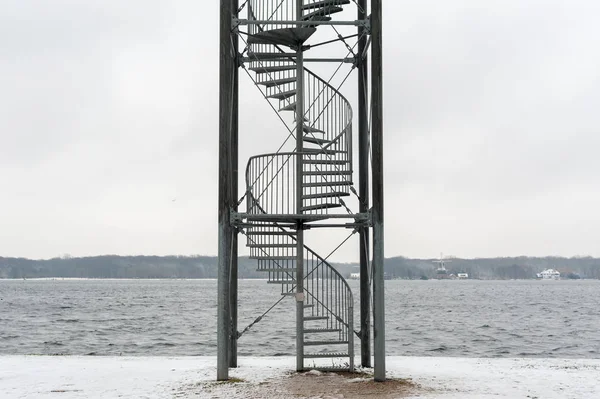 Escadas de aço espiral sob a neve com um lago no fundo — Fotografia de Stock