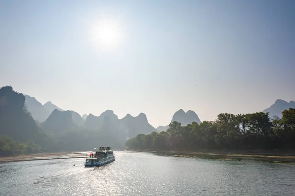 Boat on Li river cruise against the sun and karst formation mountain landscape in Guilin