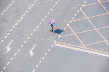 Kavşakta şemsiyeli yaşlı Çinli bir adam yürüyor.