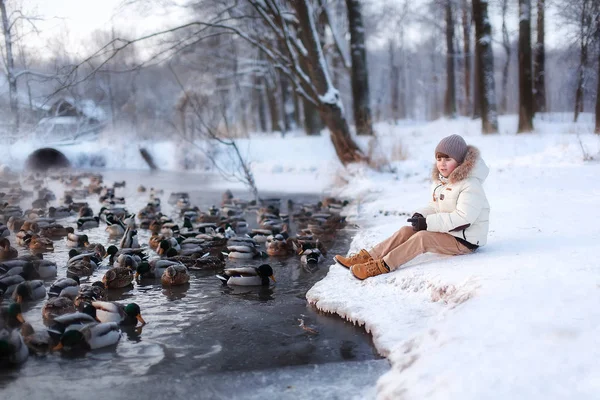Enfant assis au bord de l'étang en hiver Photo De Stock