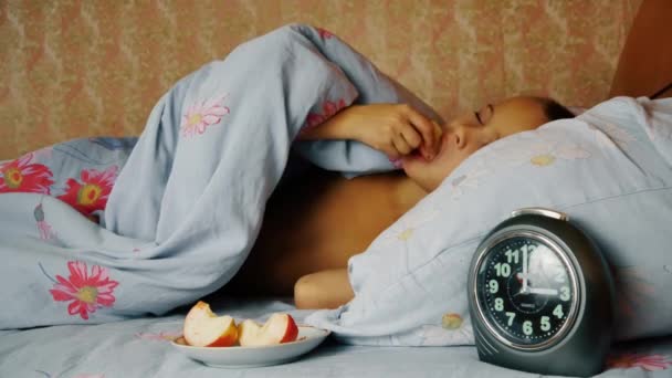 Niño en la cama se despierta por la noche del hambre y come manzanas — Vídeos de Stock