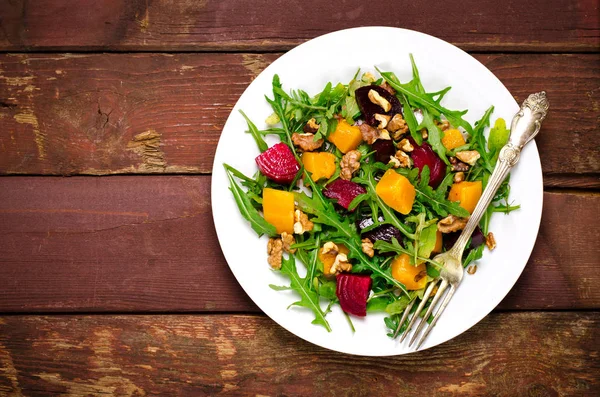 Herbstsalat mit Gemüse, Rucola, Walnüssen, Roter Bete und geröstetem Kürbis, Kürbis auf Holzgrund — Stockfoto