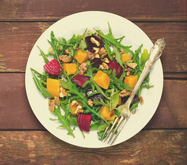Salada de outono com verduras, rúcula, nozes, beterraba e abóbora assada, abóbora sobre fundo de madeira — Fotografia de Stock