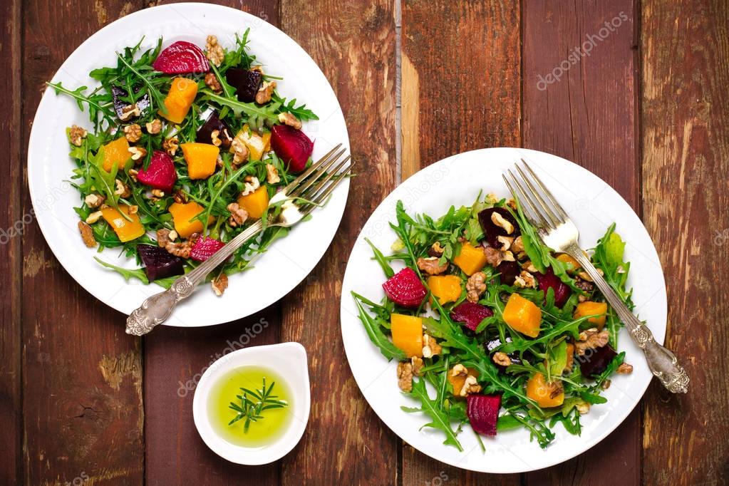 Fall salad with greens, arugula, walnuts, beetroot and roasted squash, pumpkin on wooden background