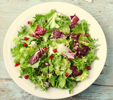 Ispanak, frisee, roka, radicchio ve nar tohumları üzerinde ahşap arka plan mavi ile yeşil salata