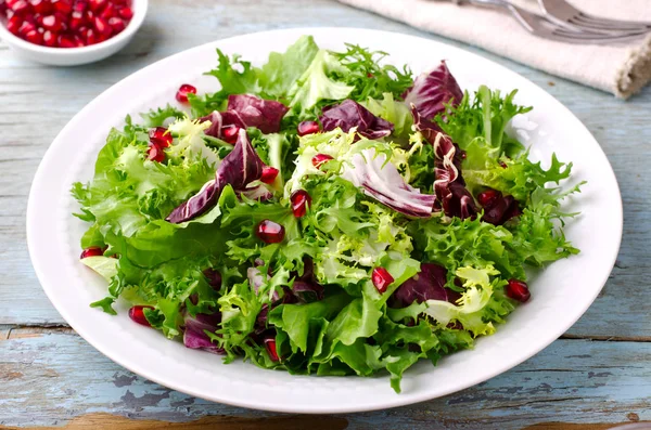 Grüner Salat mit Spinat, Frisee, Rucola, Radicchio und Granatapfelkernen auf blauem Holzgrund — Stockfoto