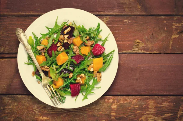 Herbstsalat mit Gemüse, Rucola, Walnüssen, Roter Bete und geröstetem Kürbis, Kürbis auf Holzgrund — Stockfoto