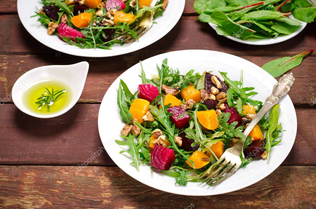 Fall salad with greens, arugula, walnuts, beetroot and roasted squash, pumpkin on wooden background