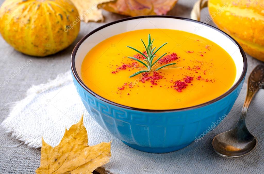 Pumpkin cream soup with rosemary and paprika in blue bowl. Halloween Thanksgiving Autumn food concept