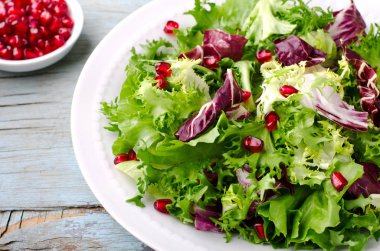 Ispanak, frisee, roka, radicchio ve nar tohumları üzerinde ahşap arka plan mavi ile yeşil salata