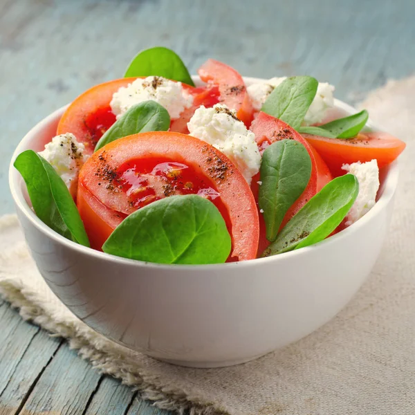 Salada de tomate com espinafre, queijo cottage, azeite e pimenta sobre fundo de madeira azul — Fotografia de Stock