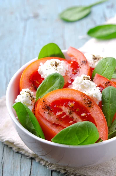 Salada de tomate com espinafre, queijo cottage, azeite e pimenta sobre fundo de madeira azul — Fotografia de Stock