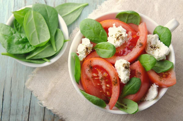 Salada de tomate com espinafre, queijo cottage, azeite e pimenta sobre fundo de madeira azul — Fotografia de Stock