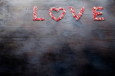 Word Love made with small candy hearts, pink, red, whie colors, on dark background. Valentines day concept. Top view, copy space.
