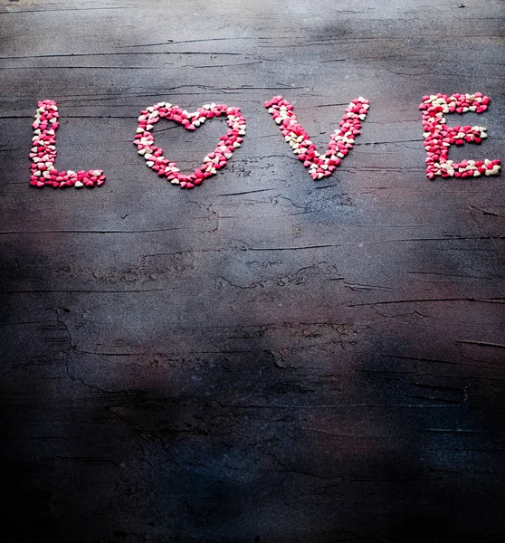 Word Love made with small candy hearts, pink, red, whie colors, on dark background. Valentines day concept. Top view, copy space. — Stok fotoğraf