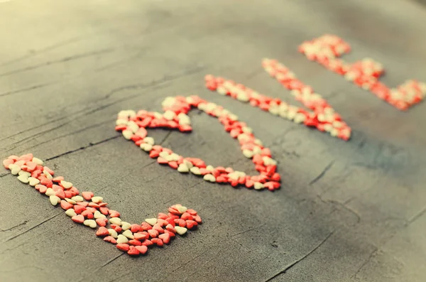 Word Love made with small candy hearts, pink, red, whie colors, on dark background. Valentines day concept. Top view, copy space. — Stok fotoğraf