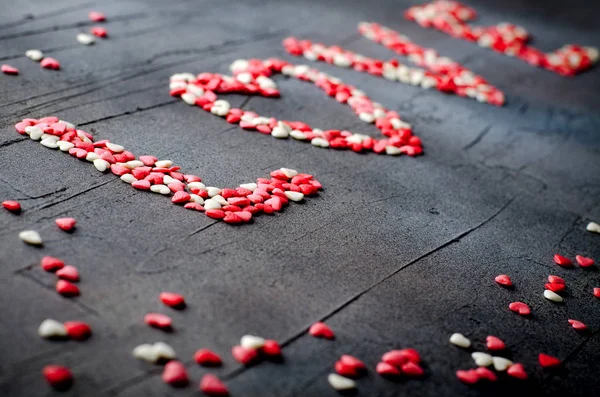 Word Love made with small candy hearts, pink, red, whie colors, on dark background. Valentines day concept. Top view, copy space. — Stok fotoğraf