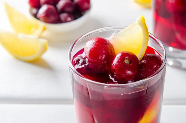 Cold drink with cherry and lemon in glasses, on white wooden background — Stock Photo, Image