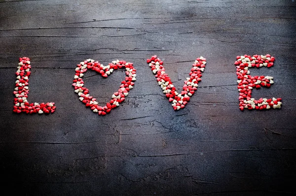 Word Love made with small candy hearts, pink, red, white colors, on dark background. Valentines day concept. Top view, copy space.