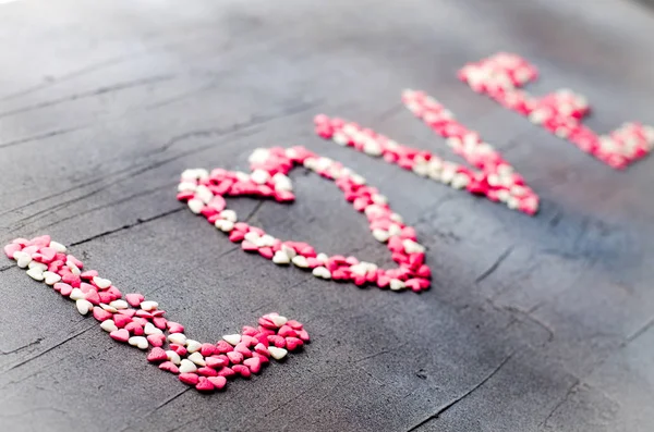 Palabra Amor hecha con pequeños corazones de caramelo, rosa, rojo, colores blancos, sobre fondo oscuro. Concepto de San Valentín. Vista superior, espacio de copia . — Foto de Stock