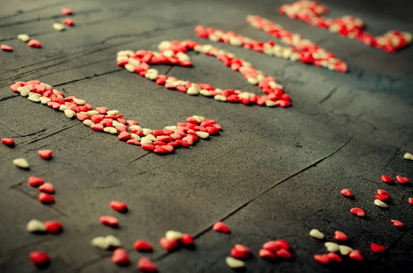 Palabra Amor hecha con pequeños corazones de caramelo, rosa, rojo, colores blancos, sobre fondo oscuro. Concepto de San Valentín. Vista superior, espacio de copia . — Foto de Stock