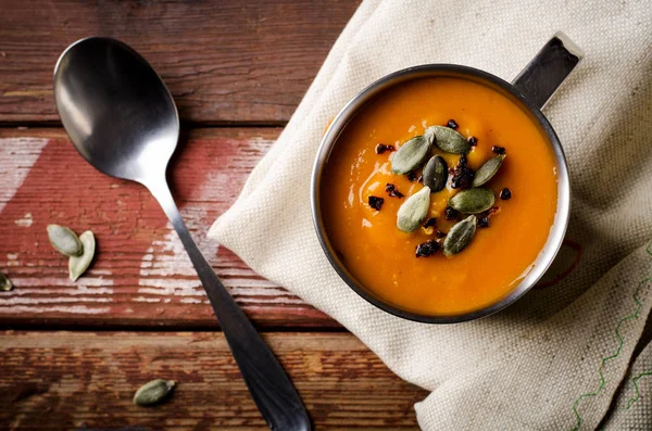 Geröstete Kürbissuppe in Metallbecher mit Kernen und geräuchertem Paprika, auf rustikalem Holzgrund. — Stockfoto