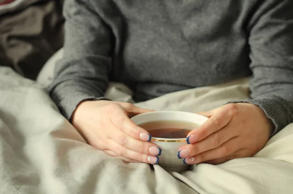 Mani femminili che tengono una tazza di tè caldo su una coperta calda . — Foto Stock