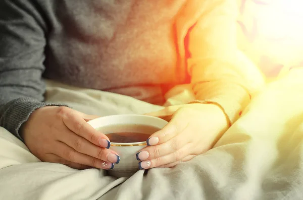 Mani femminili che tengono una tazza di tè caldo su una coperta calda . — Foto Stock