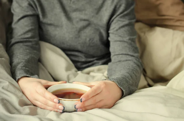 Mani femminili che tengono una tazza di tè caldo su una coperta calda . — Foto Stock