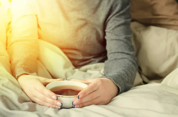 Mani femminili che tengono una tazza di tè caldo su una coperta calda . — Foto Stock