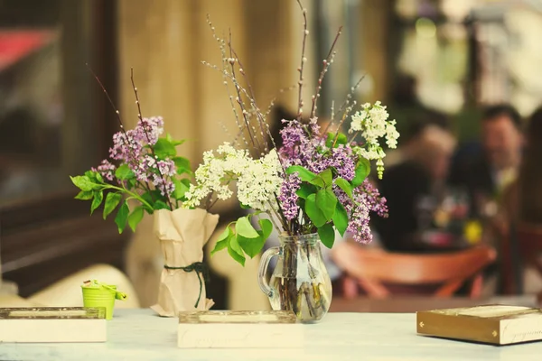 Rama con flores frescas de primavera lila en jarrón, en la mesa en el café — Foto de Stock