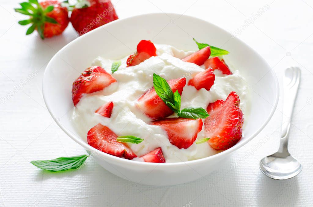 Breakfast with bowl of thick organic greek yogurt and fresh strawberries on white backgfound