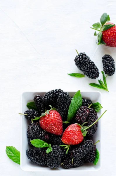 Mulberries maduras frescas e morangos com hortelã em tigela sobre fundo branco, espaço cópia — Fotografia de Stock