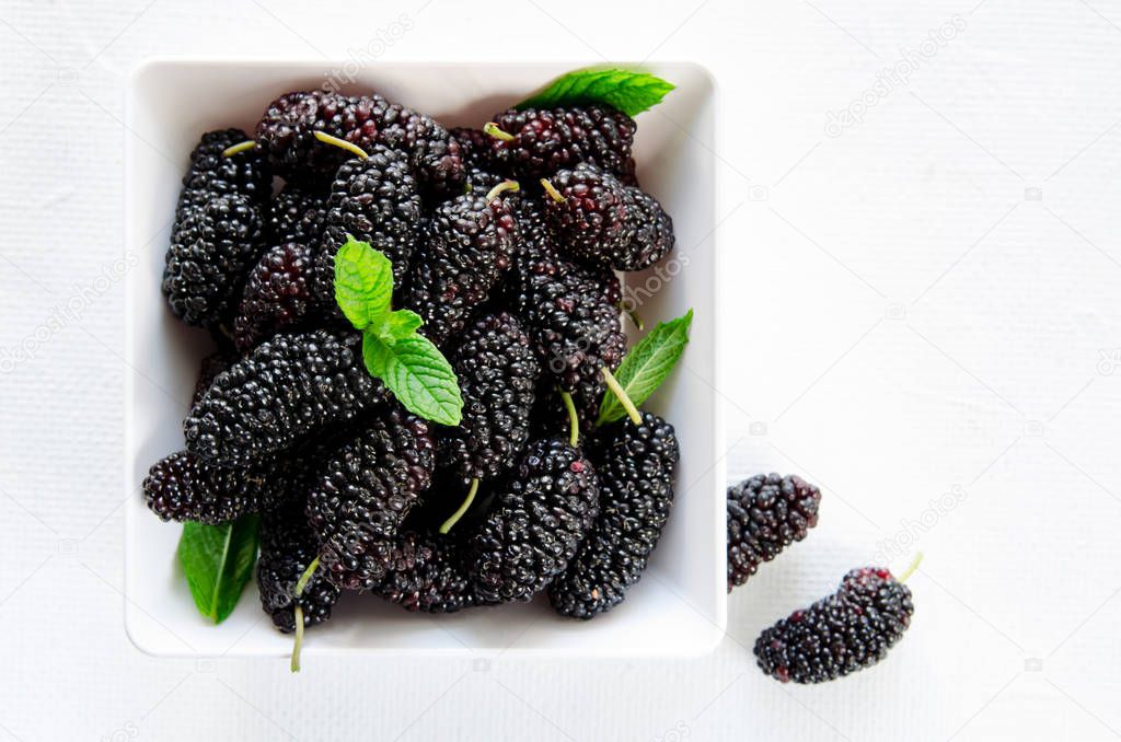 Fresh ripe mulberries with mint in bowl on white background, copy space