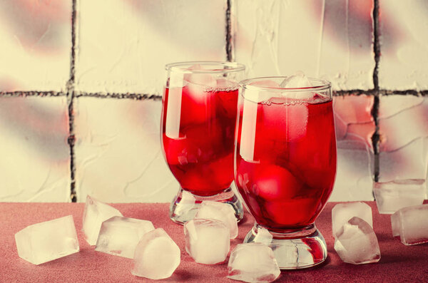 Cold cherry drink with ice cubes in glasses, on pink background