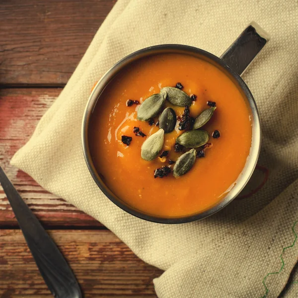 Tohum ve rustik ahşap arka plan üzerinde füme kırmızı biber ile metal mug içinde kavrulmuş balkabağı çorbası.