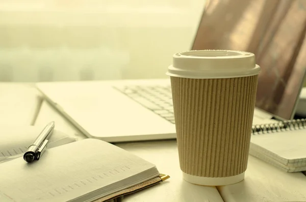 Taza de papel de café en la mesa de trabajo con cosas de oficina, bloc de notas, computadora portátil, pluma y taza de café —  Fotos de Stock