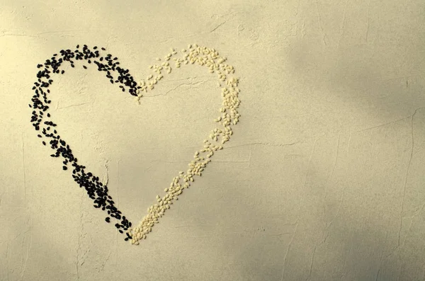Coração feito com sementes de sésamo preto e branco, sobre fundo cinza. Amor, conceito do dia dos namorados. Vista superior, espaço de cópia . Imagens Royalty-Free