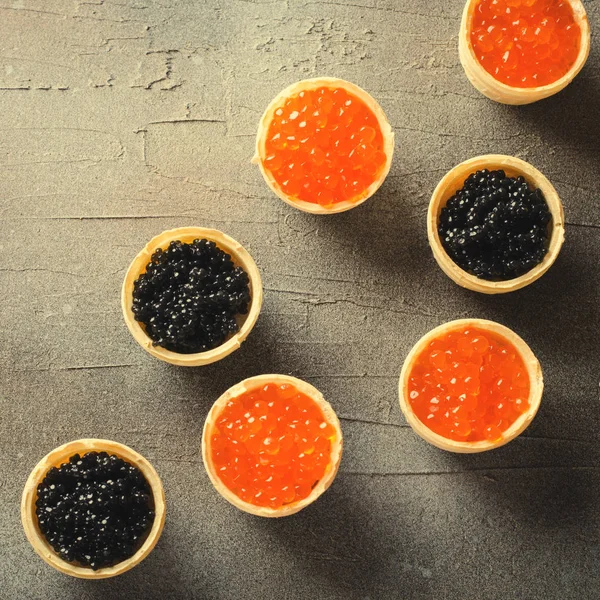 Tartes de caviar preto e vermelho, aperitivo canapés em fundo cinza, vista superior, tonificado — Fotografia de Stock