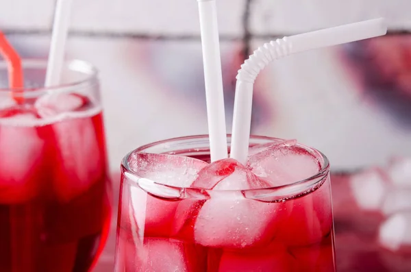 Холодний вишневий напій з кубиками льоду і трубками коктейлів в окулярах, на рожевому фоні — стокове фото