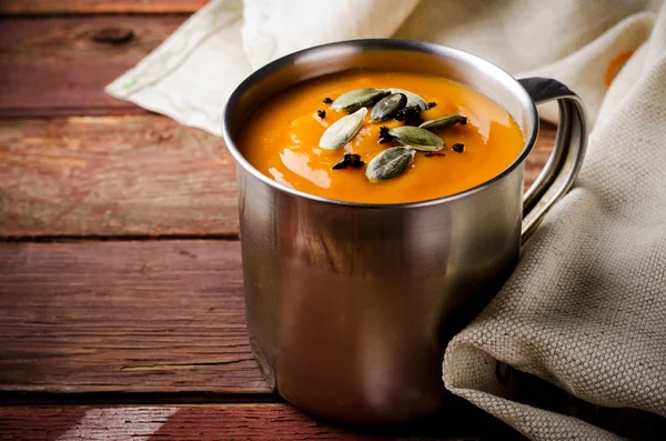 Geröstete Kürbissuppe in Metallbecher mit Kernen und geräuchertem Paprika, auf rustikalem Holzgrund. — Stockfoto